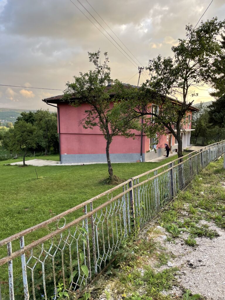 Rotfarbenes Einfamilienhaus mit gepflegtem Garten und Metallzaun bei Sonnenuntergang in Šipovo