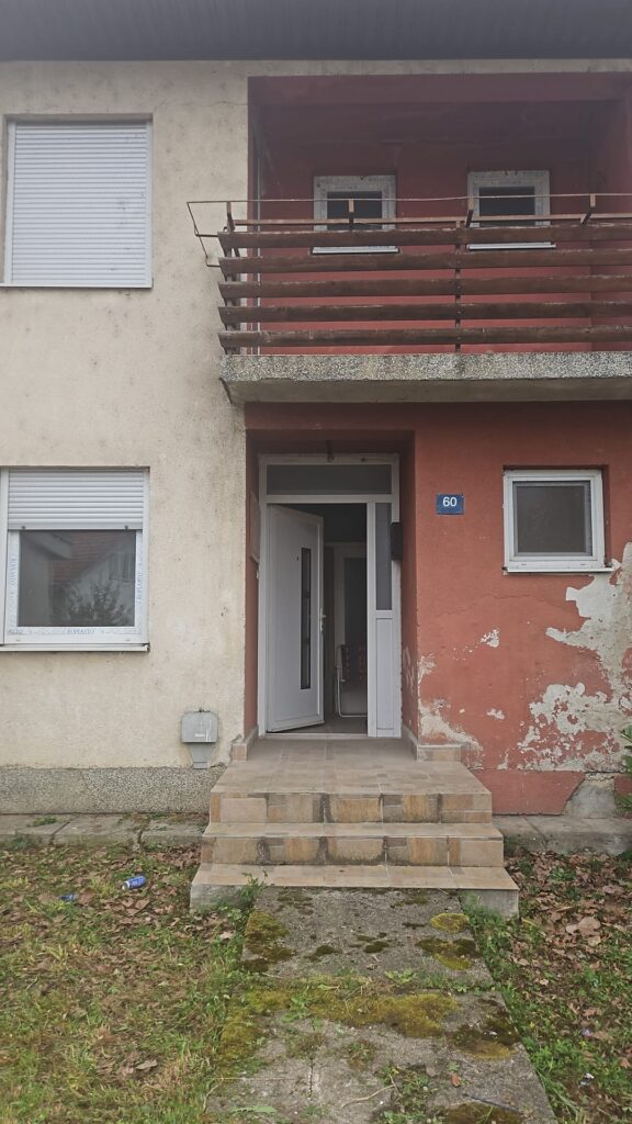 Verwittertes Wohnhaus mit rotfarbener Fassade und überdachtem Balkon in Banja Luka, Bosnien