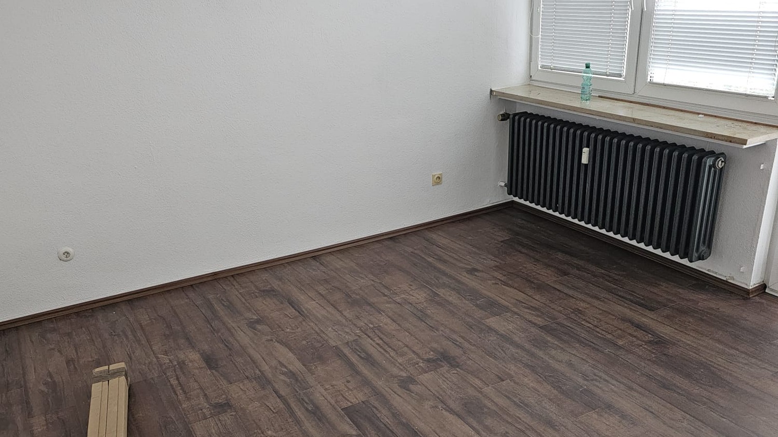 Leeres Zimmer mit frisch verlegtem Holzboden, altem Heizkörper und Fenster während der Wohnungssanierung in Nürnberg